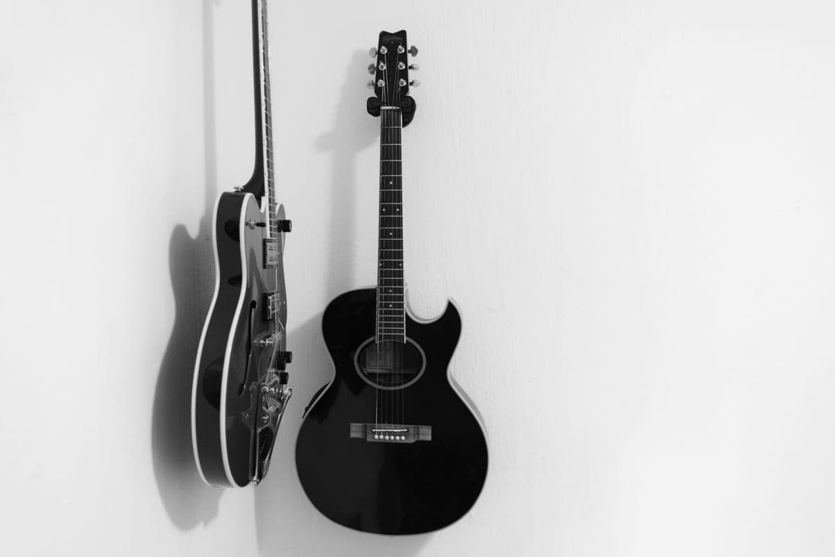 An acoustic guitar resting against a pale wall in daylight